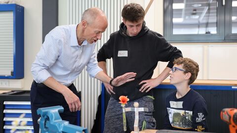 Bildungsminister Schwarz steht neben einem Tisch an dem ein junge mit seinem Projekt sitzt. Daneben steht ein Jugendlicher.