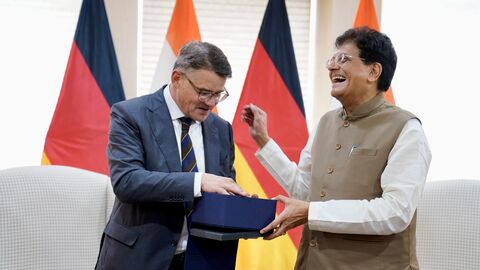 Ministerpräsident Boris Rhein trägt einen Anzug und hält mit dem indischen Minister Piyush Goyal eine Box hoch.