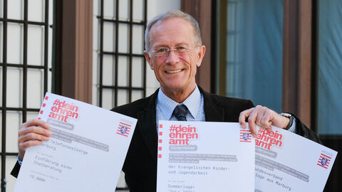 Staatsminister Axel Wintermeyer hält Förderbescheide in die Kamera