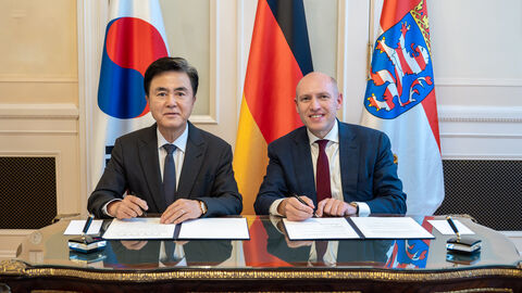 Manfred Pentz mit dem Gouverneur der Region Chungnam, S.E. Taeheum KIM Zwei Männer sitzen am Schreibtisch. Im Hintergrund sind die koreanische, die deutsche und die hessische Flagge zu sehen.